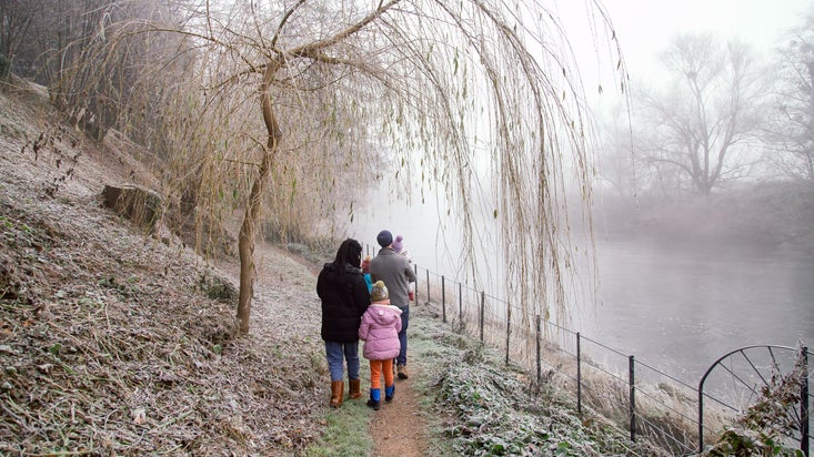 Family walking by the river, surrounded by mist and frost-covered trees.
